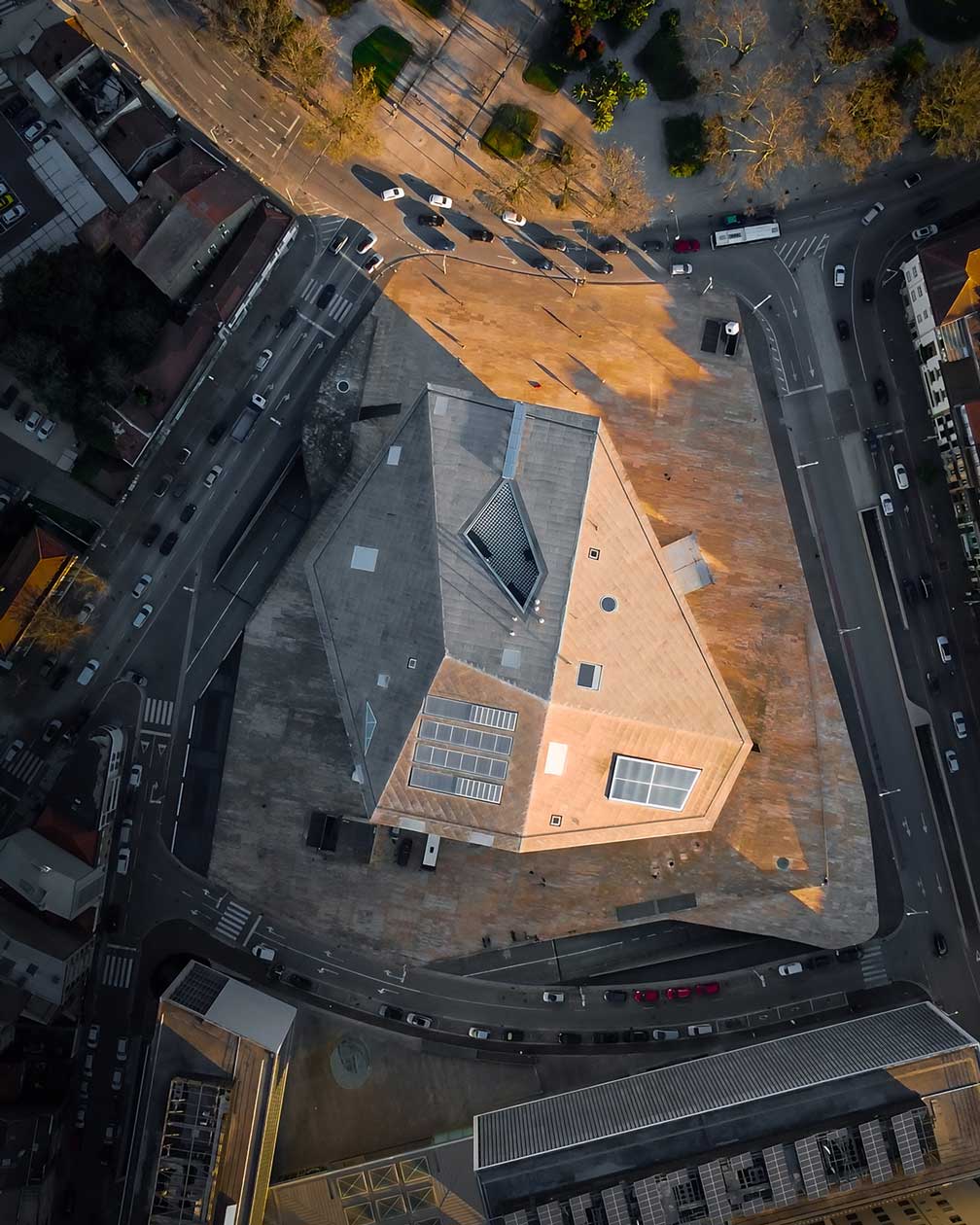 Vista aérea da Casa da Música no Porto ao pôr do sol, captada por drone, com luz dourada sobre a arquitetura moderna do edifício.
