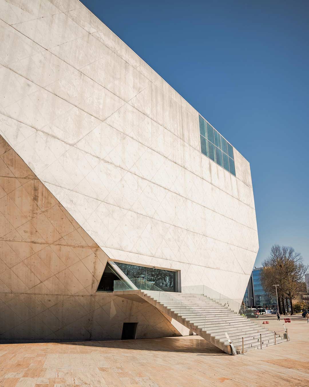 Entrada da Casa da Música numa manhã de sol, com céu limpo e luz natural a destacar as formas modernas do edifício e a sua imponência arquitetónica