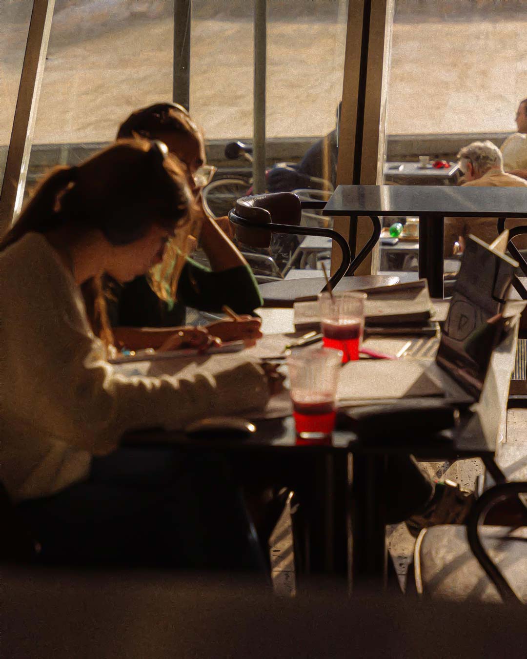Pessoas a estudar ou trabalhar no café da Casa da Música, com luz dourada do pôr do sol a entrar pelas janelas e a criar um ambiente calmo e inspirador.