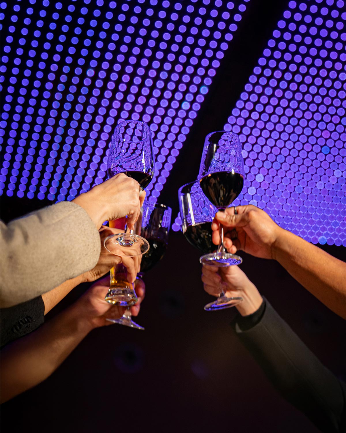Pessoas a brindar com copos de vinho no interior da Casa da Música, sob um teto roxo que cria uma atmosfera intimista e vibrante.