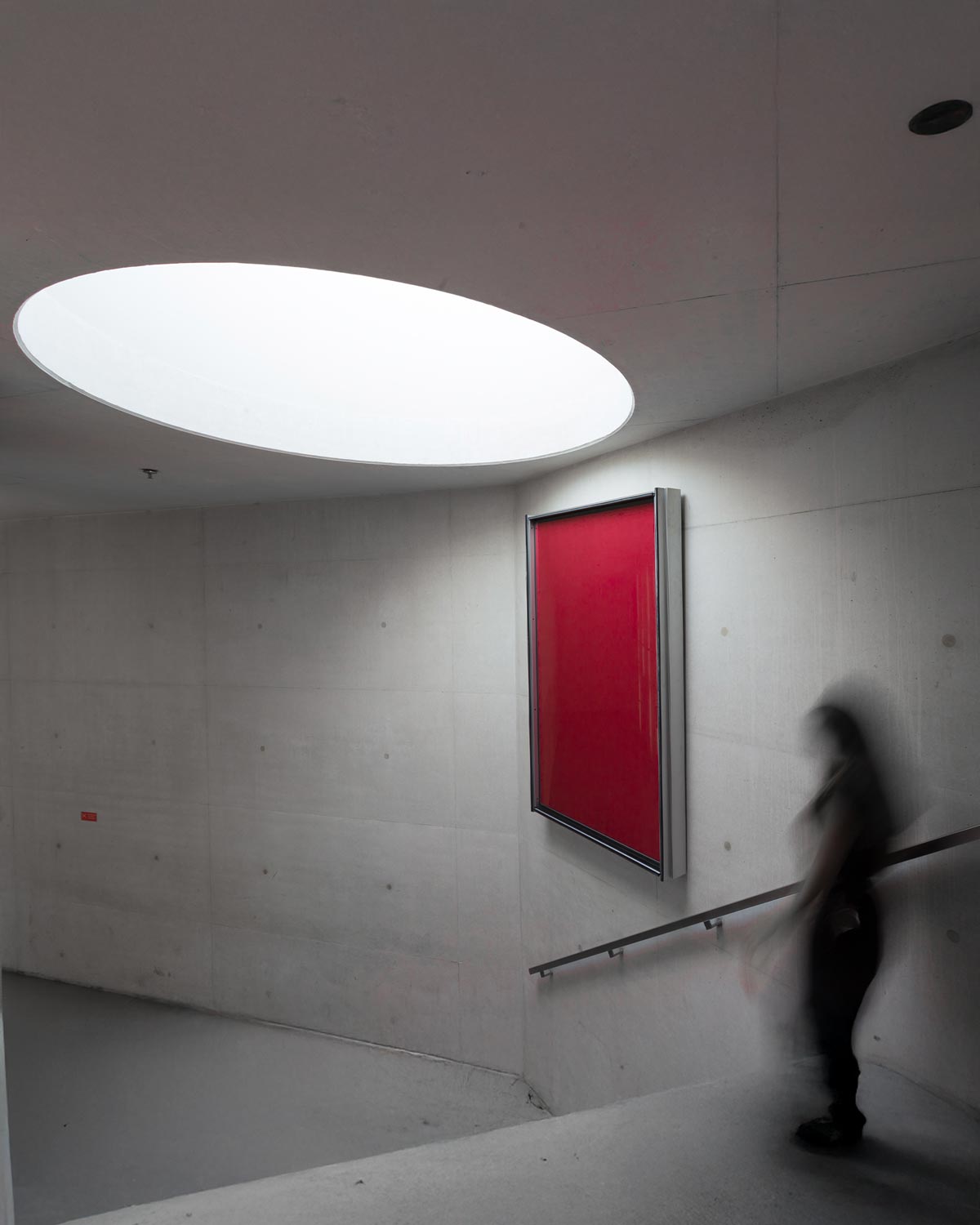 Interior da Casa da Música em cimento aparente, com luz natural, um quadro vermelho e parte das escadas visível.