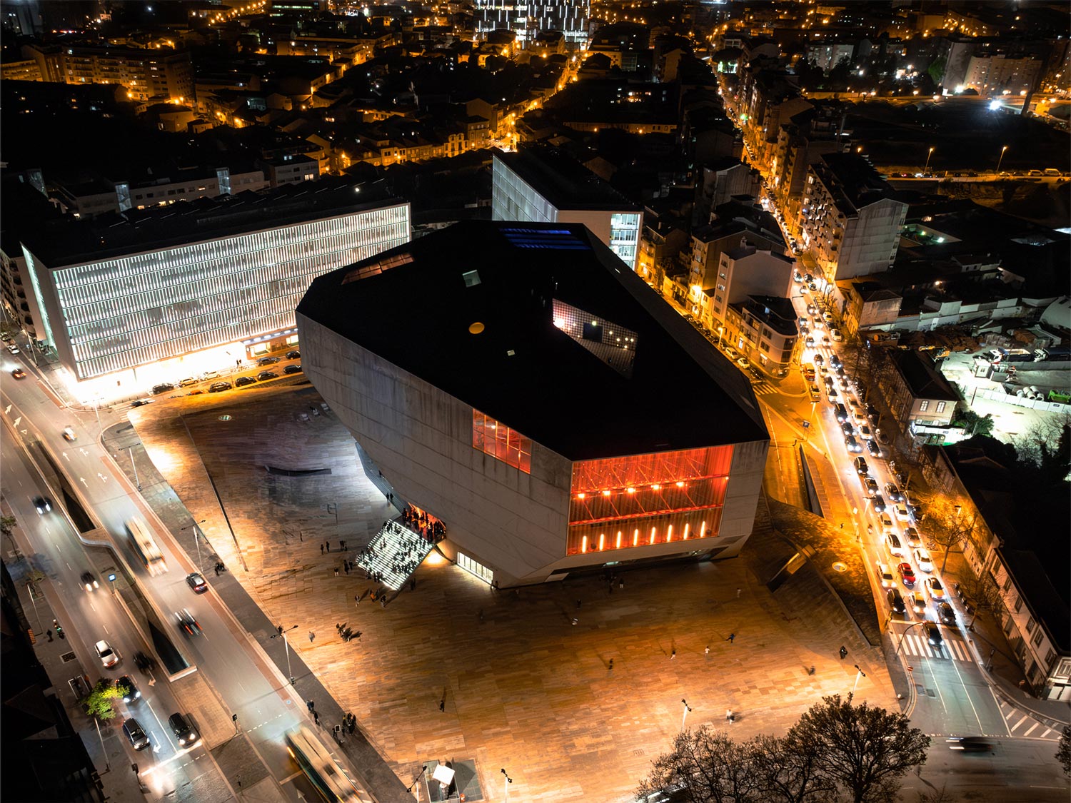 Vista aérea noturna da Casa da Música iluminada no Porto, com luzes da cidade ao fundo.