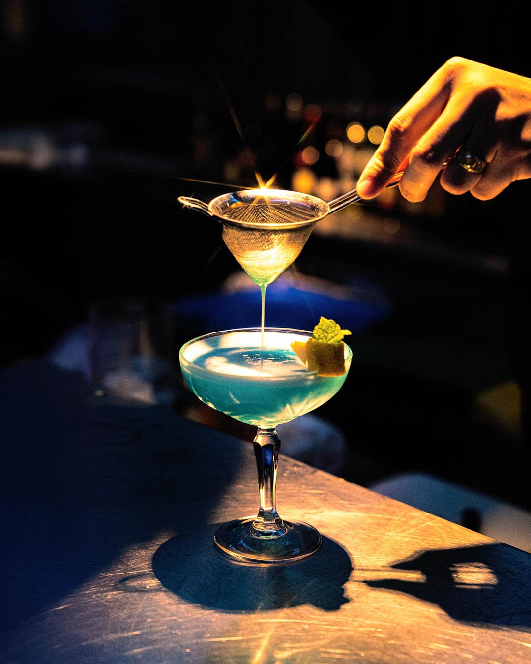 Cocktail a ser preparado no bar do MAIS, com luz suave e bonita a realçar os tons da bebida e o gesto do bartender.