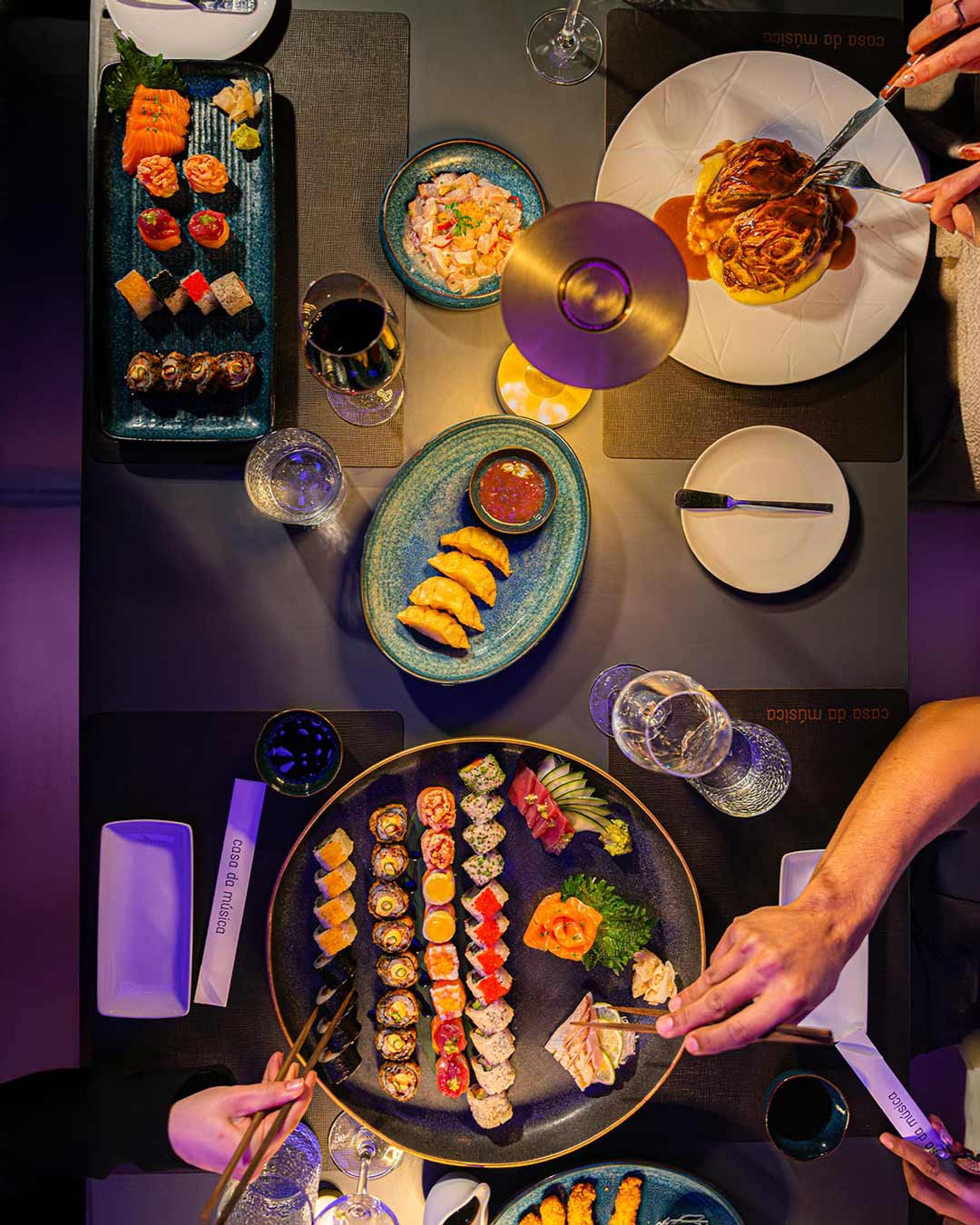 Pratos de sushi visto de cima no restaurante da Casa da Música, com as mãos de duas pessoas prestes a partilhar a refeição